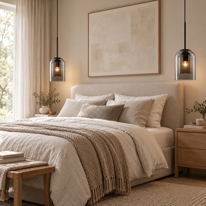 A beautifully styled bedroom featuring a bed dressed in neutral beige and cream linens with a textured throw blanket. Two modern glass pendant lights hang symmetrically above the bed, flanking a large abstract canvas painting on the beige wall.