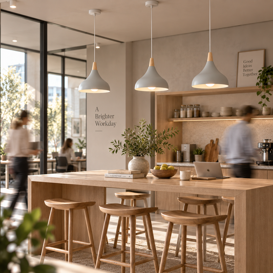A bright, modern kitchen and dining area with three white pendant lights hanging over a light wood island table with wooden stools. Blurred people are visible in the background near shelves and windows, and the space has a warm, inviting aesthetic.