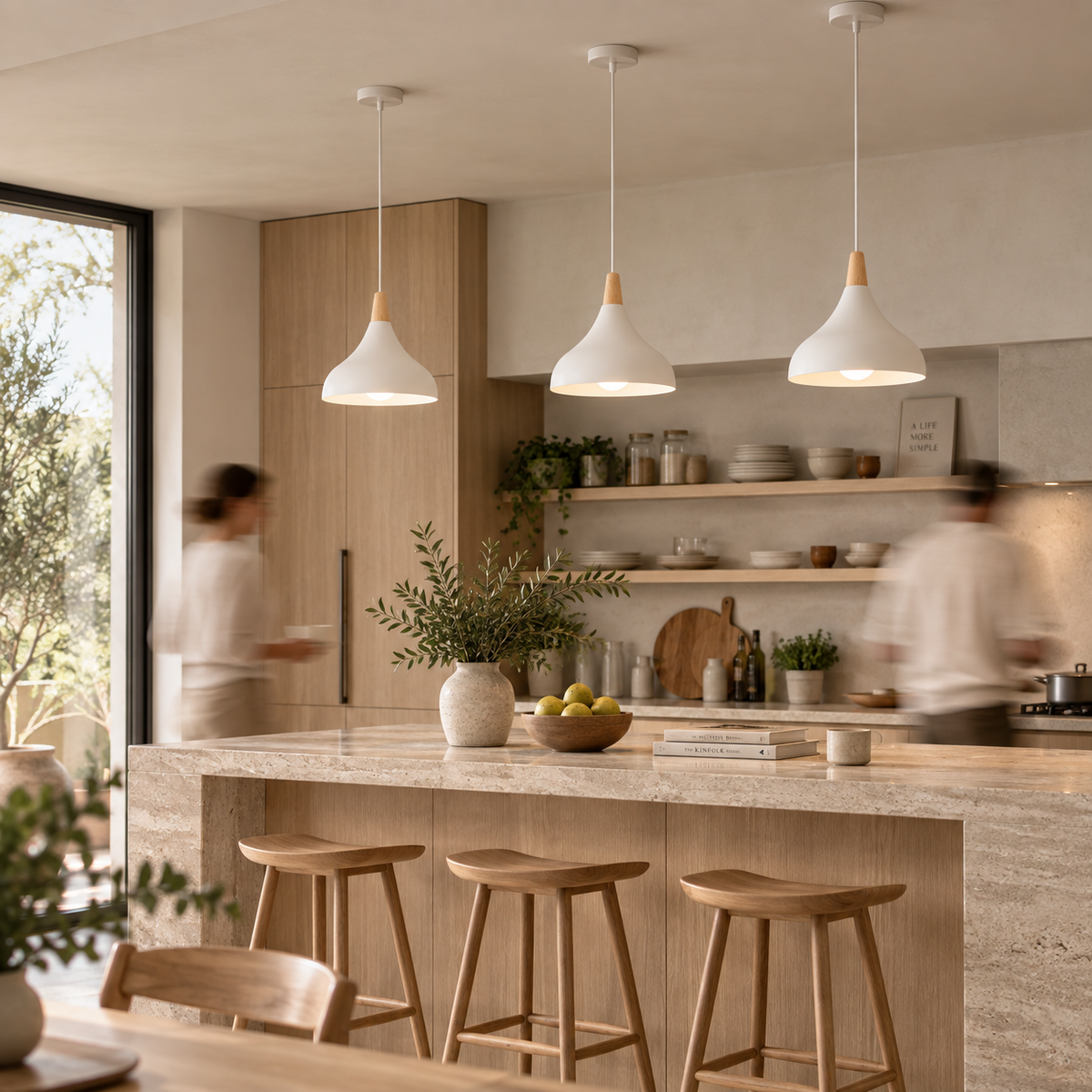 Three white pendant lights with light wood cone-shaped shades hang over a modern kitchen island with wooden stools, set in a bright, contemporary kitchen with blurred people in the background.