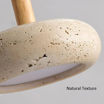 Close-up of a textured stone lamp base in a natural beige color with a light wood stem, showing the porous stone surface and the text 'Natural Texture' on a neutral gray background.