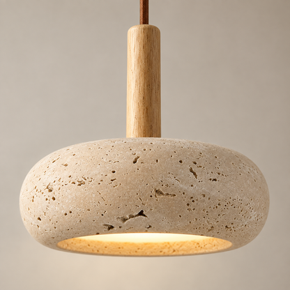 A modern pendant light fixture featuring a textured beige travertine stone shade, a natural wood stem, and a warm glowing light underneath, suspended against a neutral beige background.