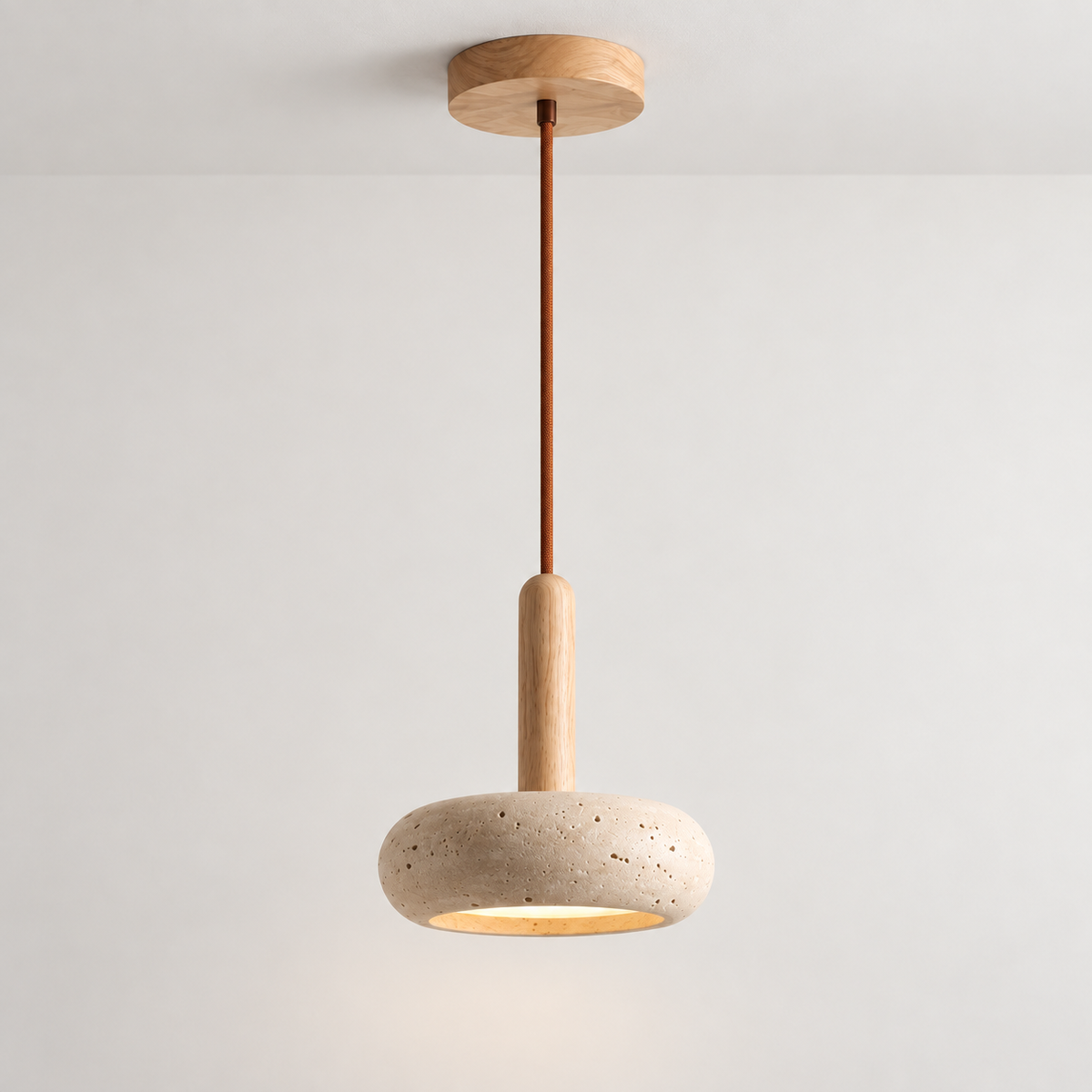 Single travertine stone pendant light with a light wood stem and bronze cord, lit and hanging against a pale wall.