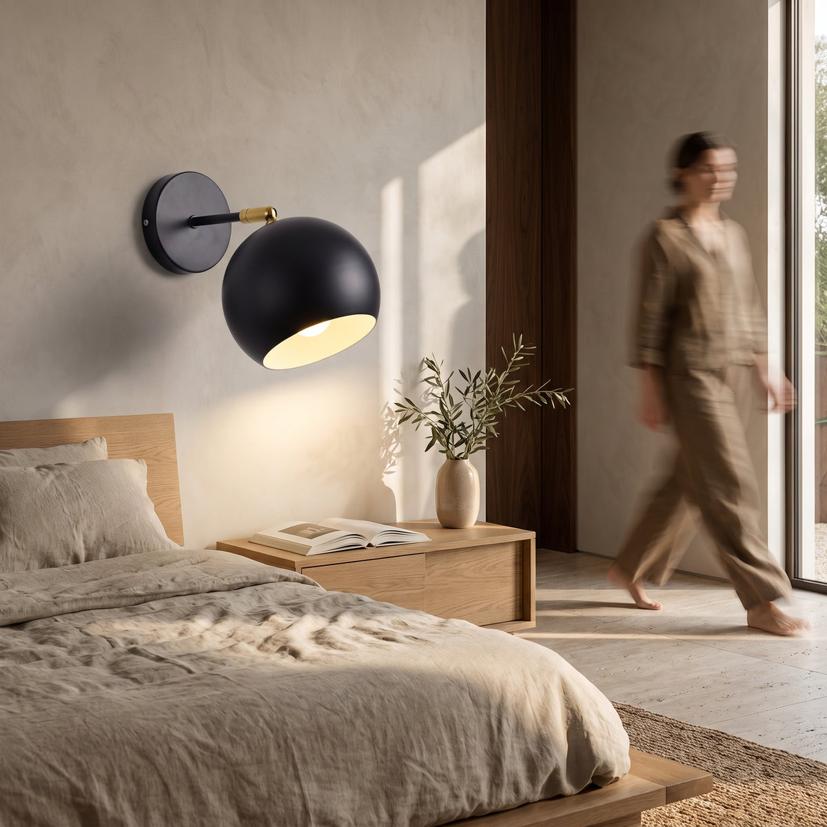 Black adjustable ball wall lamp mounted beside an oak bed with linen bedding, tilted down over an open book