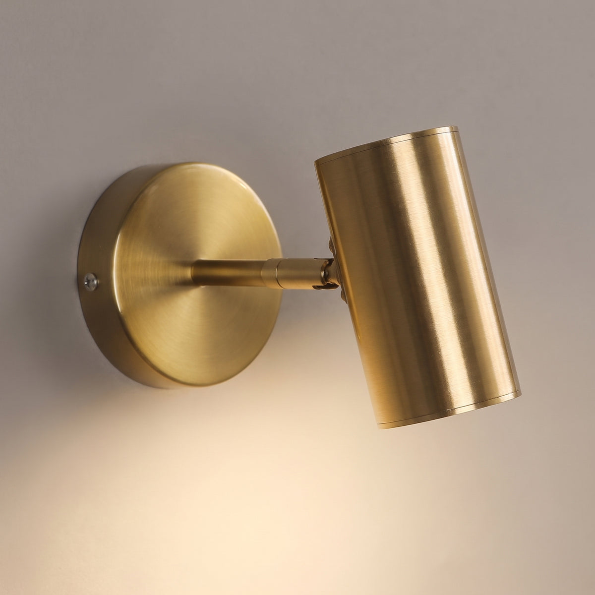 Close-up of the brushed gold wall spot light showing the machined swivel joint, round wall plate and recessed diffuser