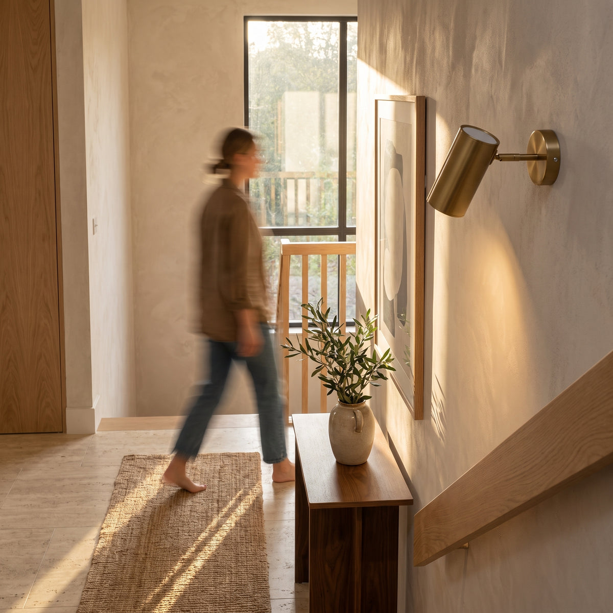 Gold adjustable wall spot light on a staircase landing, angled to wash light across a limewash plaster wall
