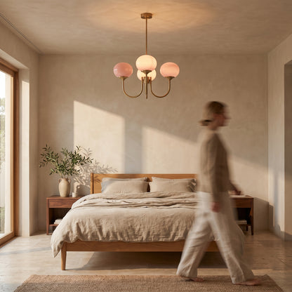 Pink three-dome glass chandelier hanging above an oak bed with linen bedding in a calm bedroom