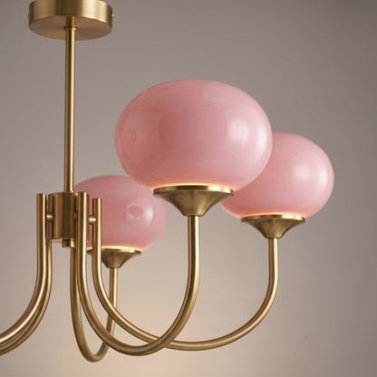 Close-up of a pink glass dome sitting on its brushed brass cup, showing the thick chalky glass and the curved arm