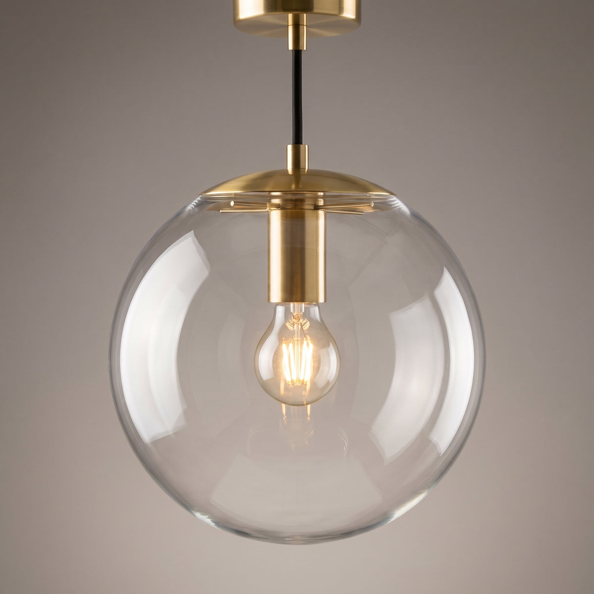 Close-up of the clear glass sphere and brushed brass collar of the globe pendant light with a glowing filament bulb inside