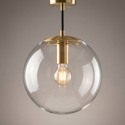 Close-up of the clear glass sphere and brushed brass collar of the globe pendant light with a glowing filament bulb inside