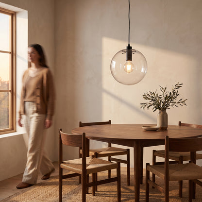 Clear glass globe pendant light with a black collar hanging above a round walnut dining table in a warm limewash dining room