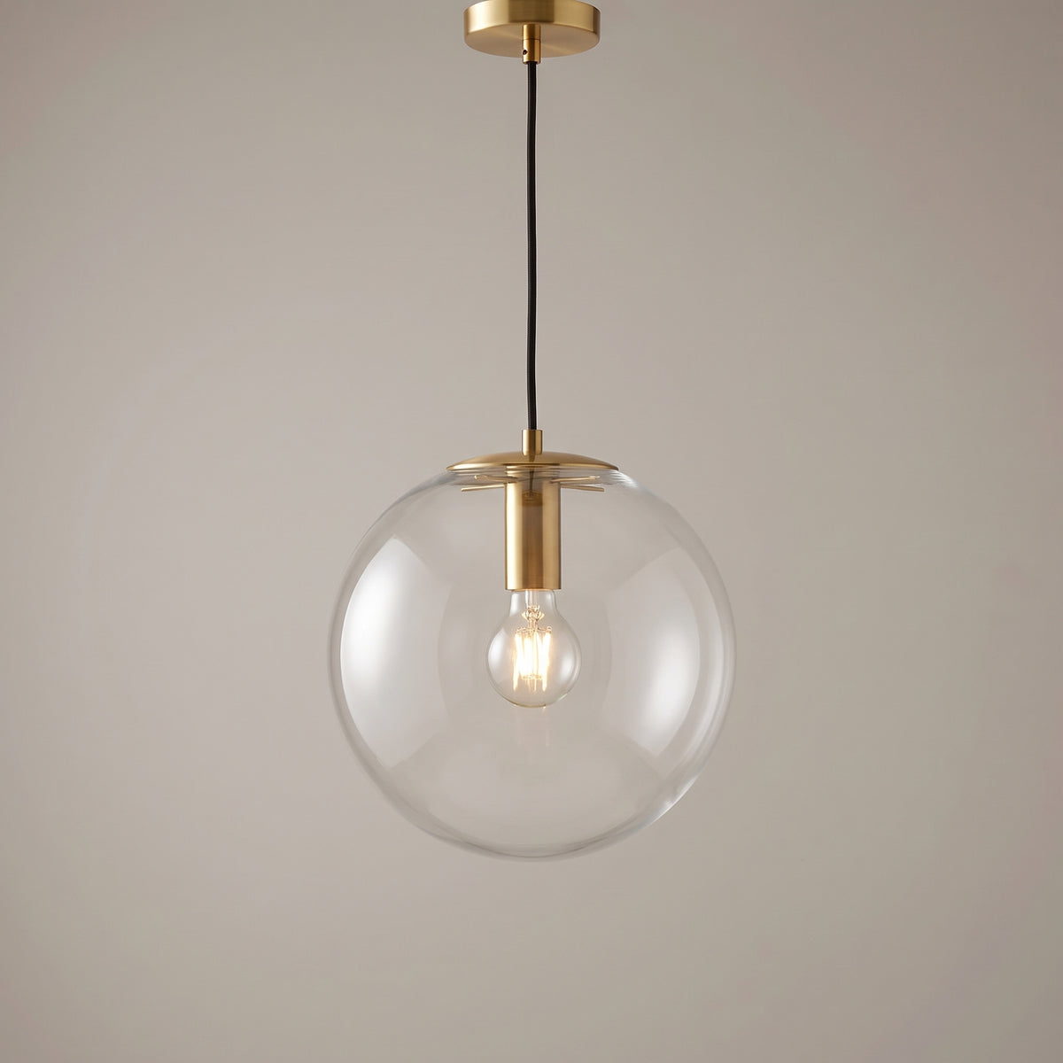 Gold finish option: clear glass globe pendant light with a polished brass collar and ceiling canopy