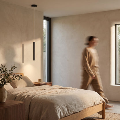Slim black tube pendant light hanging beside an oak bed above a walnut nightstand in a calm bedroom