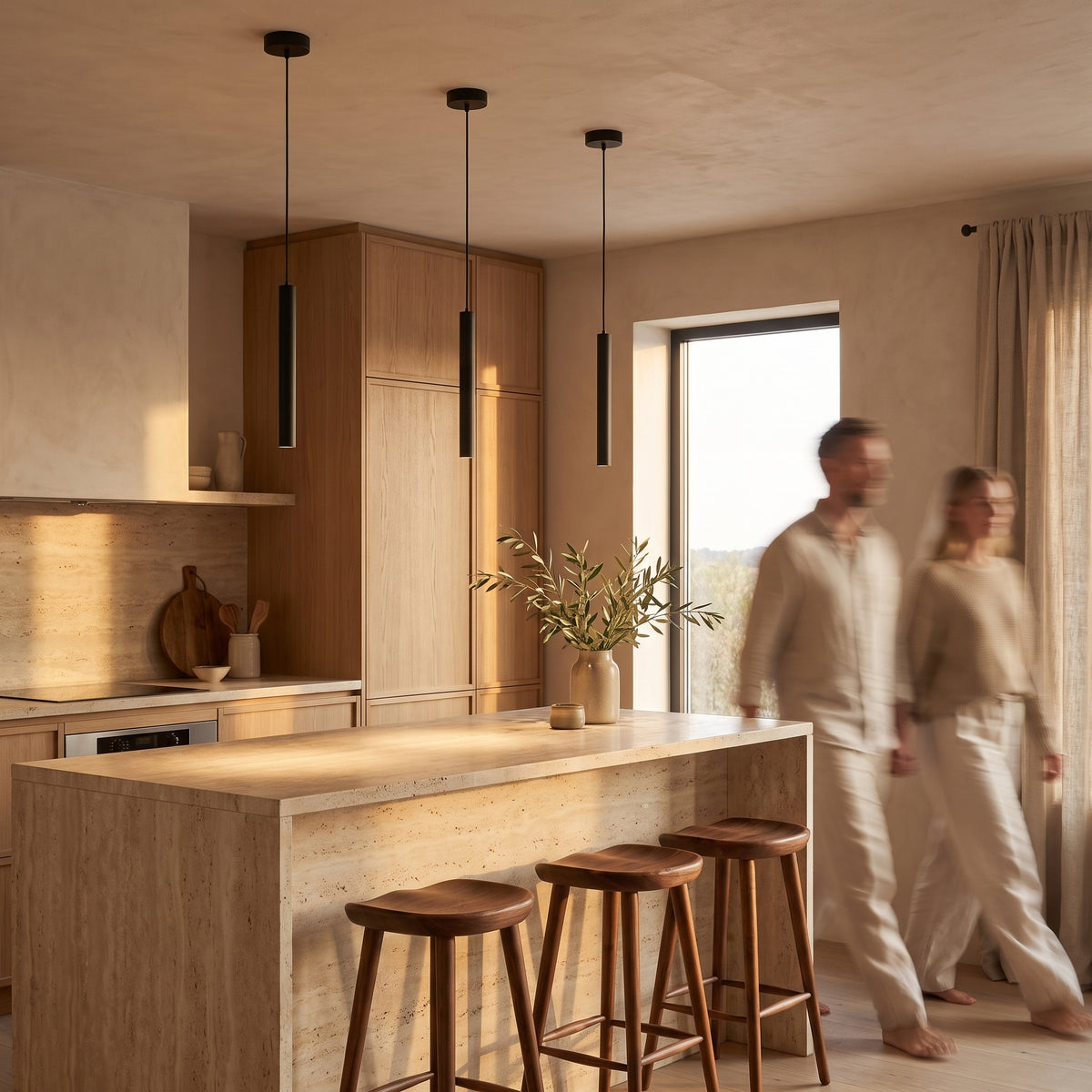 Three slim black tube pendant lights hung in a row above a travertine kitchen island with walnut bar stools