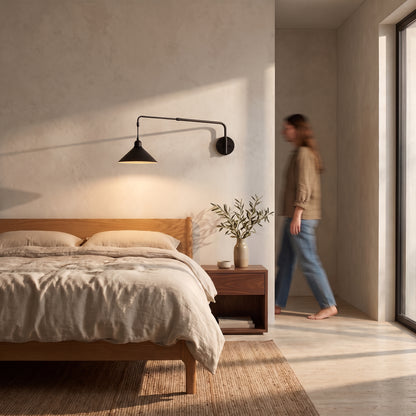 Black swing arm wall light mounted beside an oak bed, the straight arm reaching out with the cone shade hanging low over the pillow