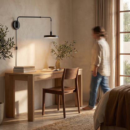 Swing arm wall light with the flat disc shade extended over a light oak desk in a home office corner