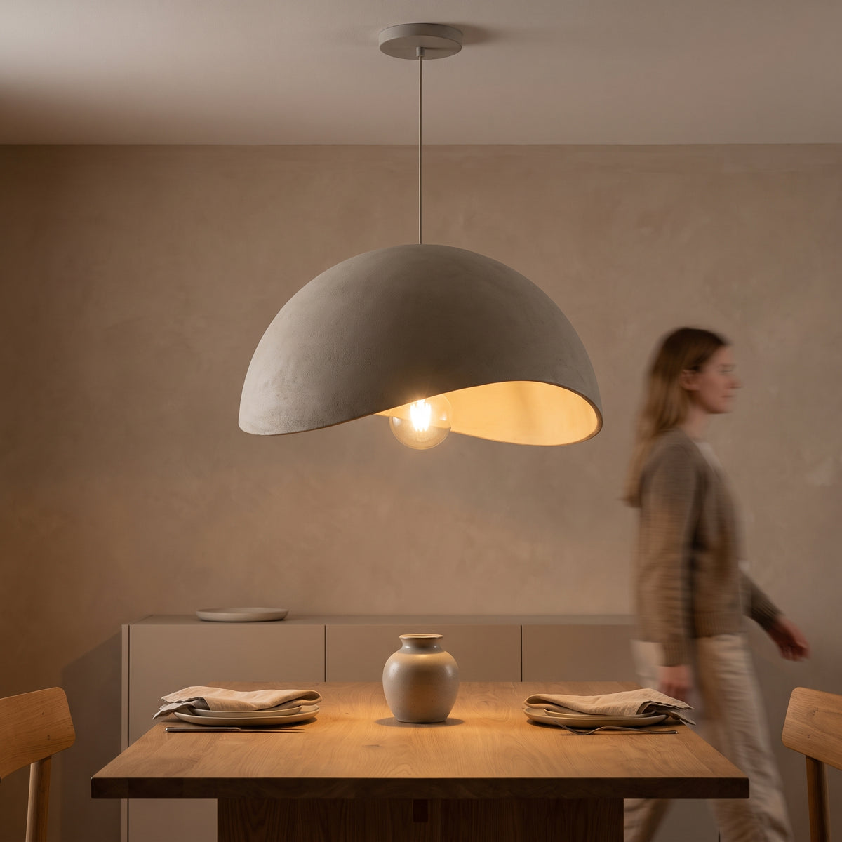 Cement grey wabi-sabi pendant lighting a wooden dining table in a plaster-walled room
