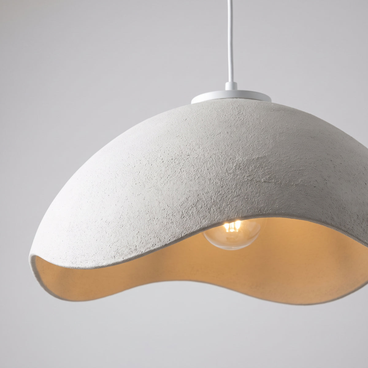 Close-up of the hand-molded plaster texture and glowing sand-gold interior of the shade
