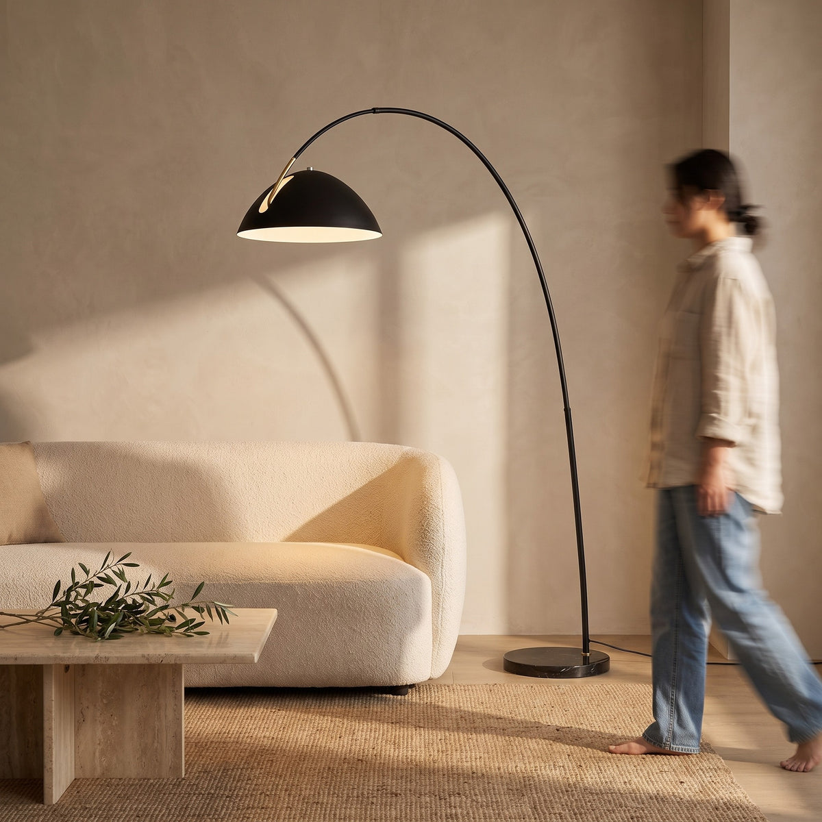 Black arc floor lamp curving over a boucle sofa in a warm living room