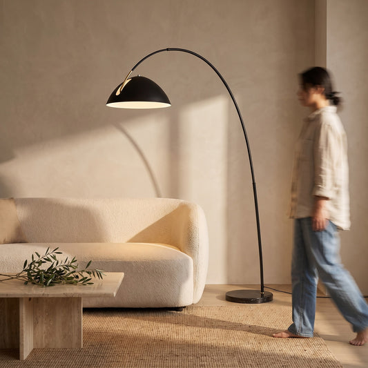 Black arc floor lamp curving over a boucle sofa in a warm living room