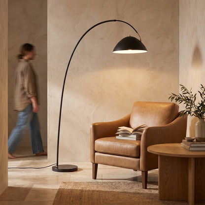 Arc floor lamp lighting a leather reading chair and side table with books