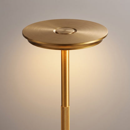 Close up of the brushed gold disc shade, touch control button and knurled stem of the cordless lamp