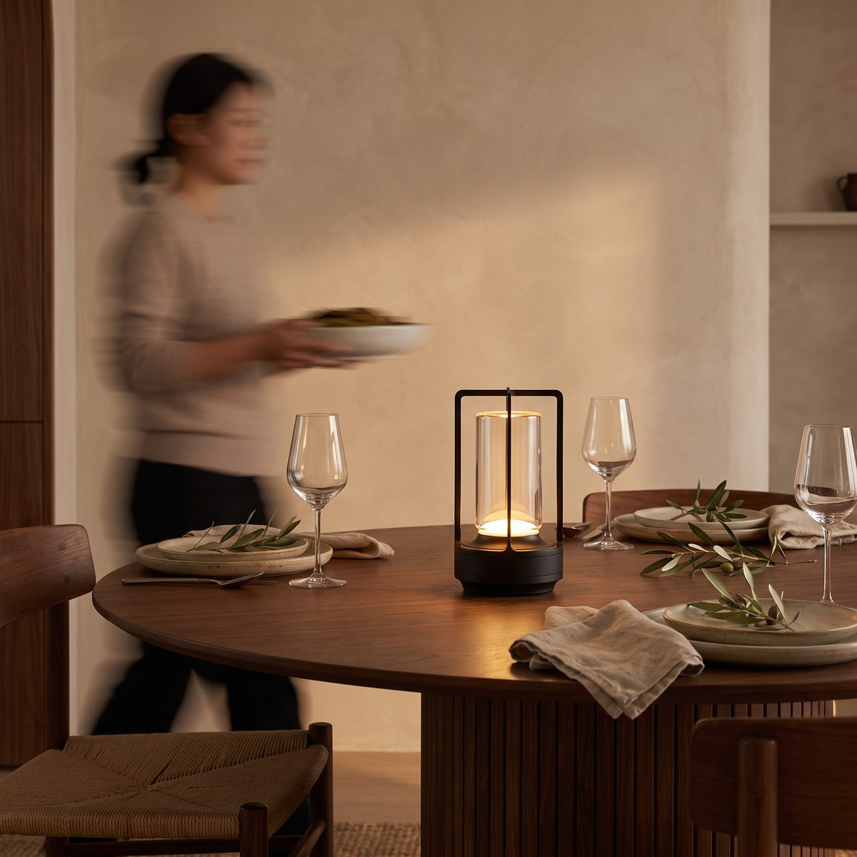 Black cordless lantern table lamp glowing on a set walnut dining table at dusk