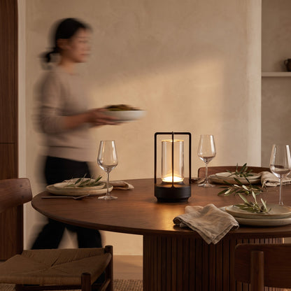 Black cordless lantern table lamp glowing on a set walnut dining table at dusk