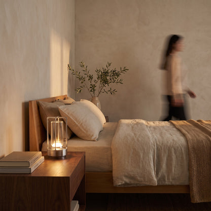 Silver cordless lantern lamp on a walnut nightstand beside a linen bed