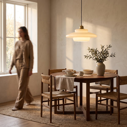 Opal glass pendant light glowing above a round walnut dining table