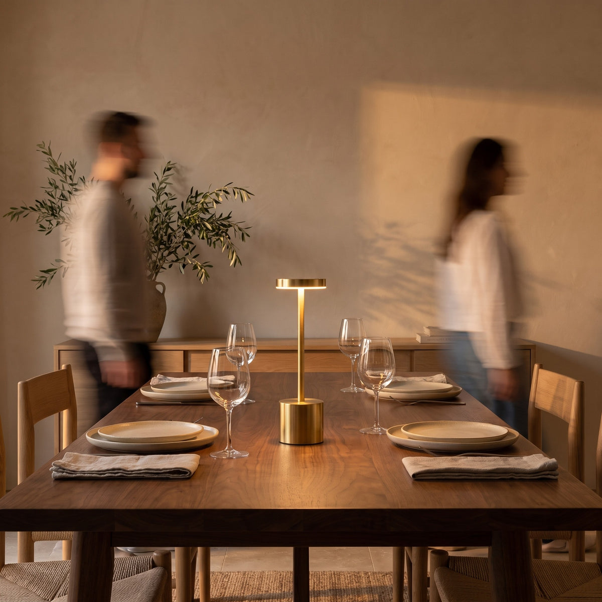 Gold slim cordless table lamp on a set walnut dining table at dusk